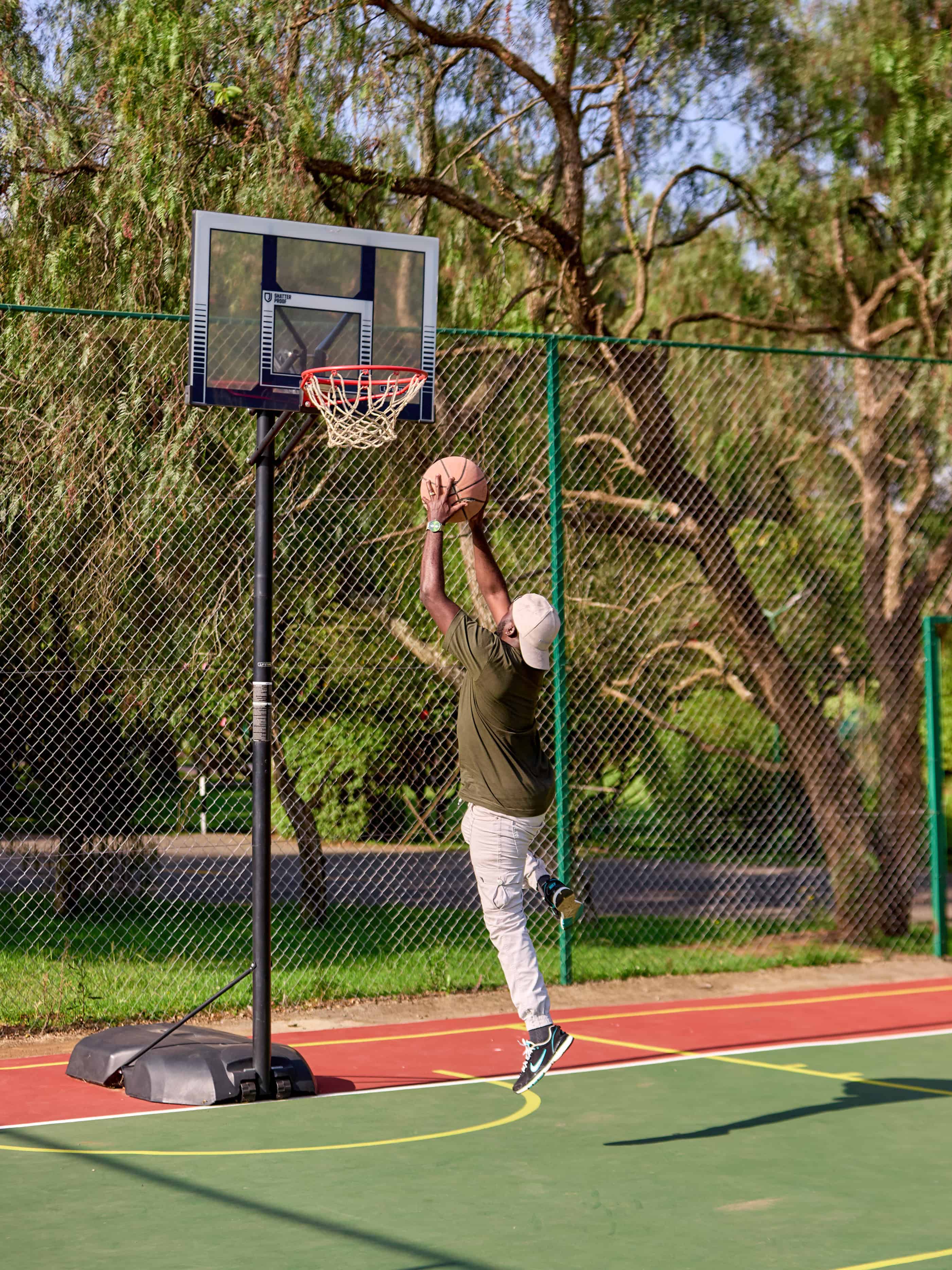Person playing basketball on outdoor court with hoop and colorful surface